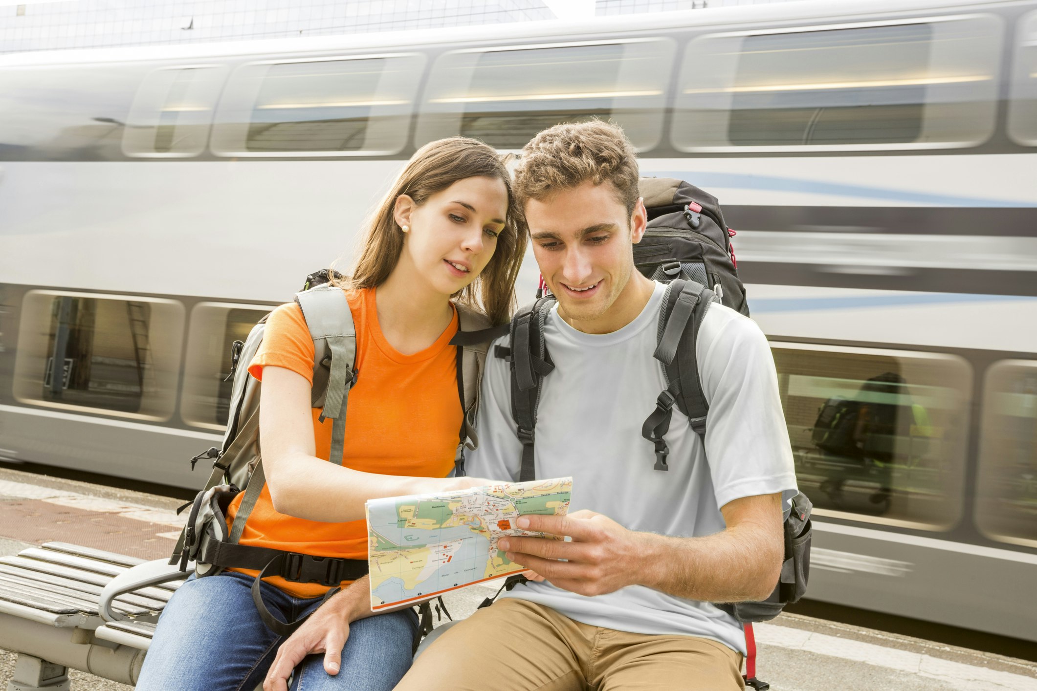 Caucasian couple sitting on bench near a train reading map