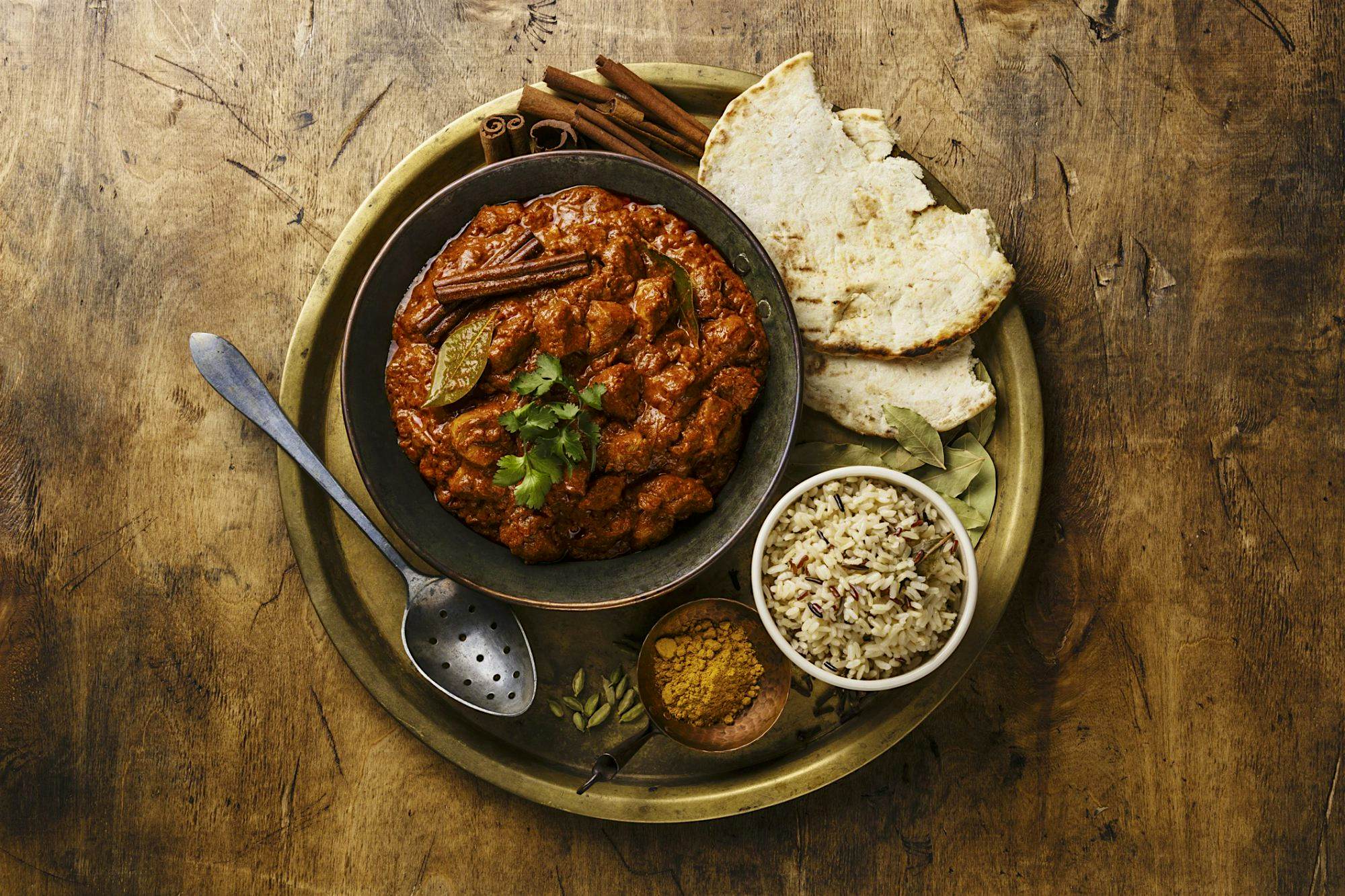 Travel News - Chicken tikka masala spicy curry meat food in copper pan with rice and naan bread on wooden background Travel News - Chicken tikka masala spicy curry meat food in copper pan with rice and naan bread on wooden background