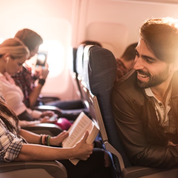 Happy passengers traveling by airplane and talking to each other. Focus is on man.