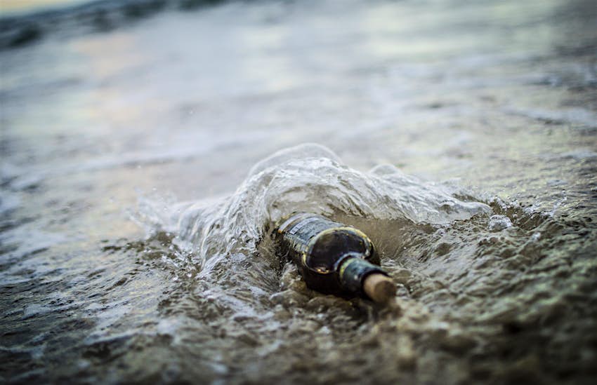 Travel News - Message in a bottle - bottle half buried in sandy beach Travel News - Message in a bottle - bottle half buried in sandy beach