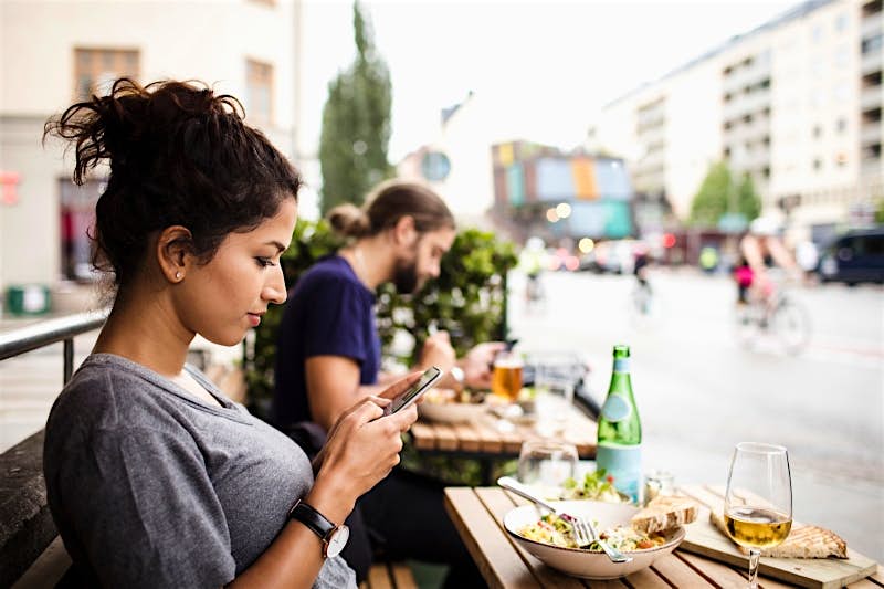 Travel News - Side view of woman text messaging while having food at sidewalk cafe in city Travel News - Side view of woman text messaging while having food at sidewalk cafe in city
