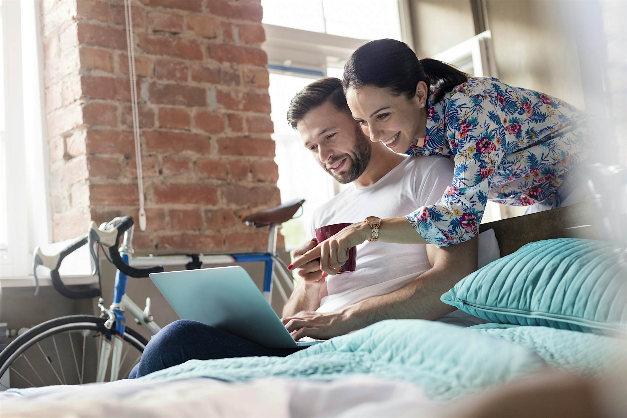Travel News - Couple drinking coffee using laptop on bed Couple drinking coffee using laptop on bed