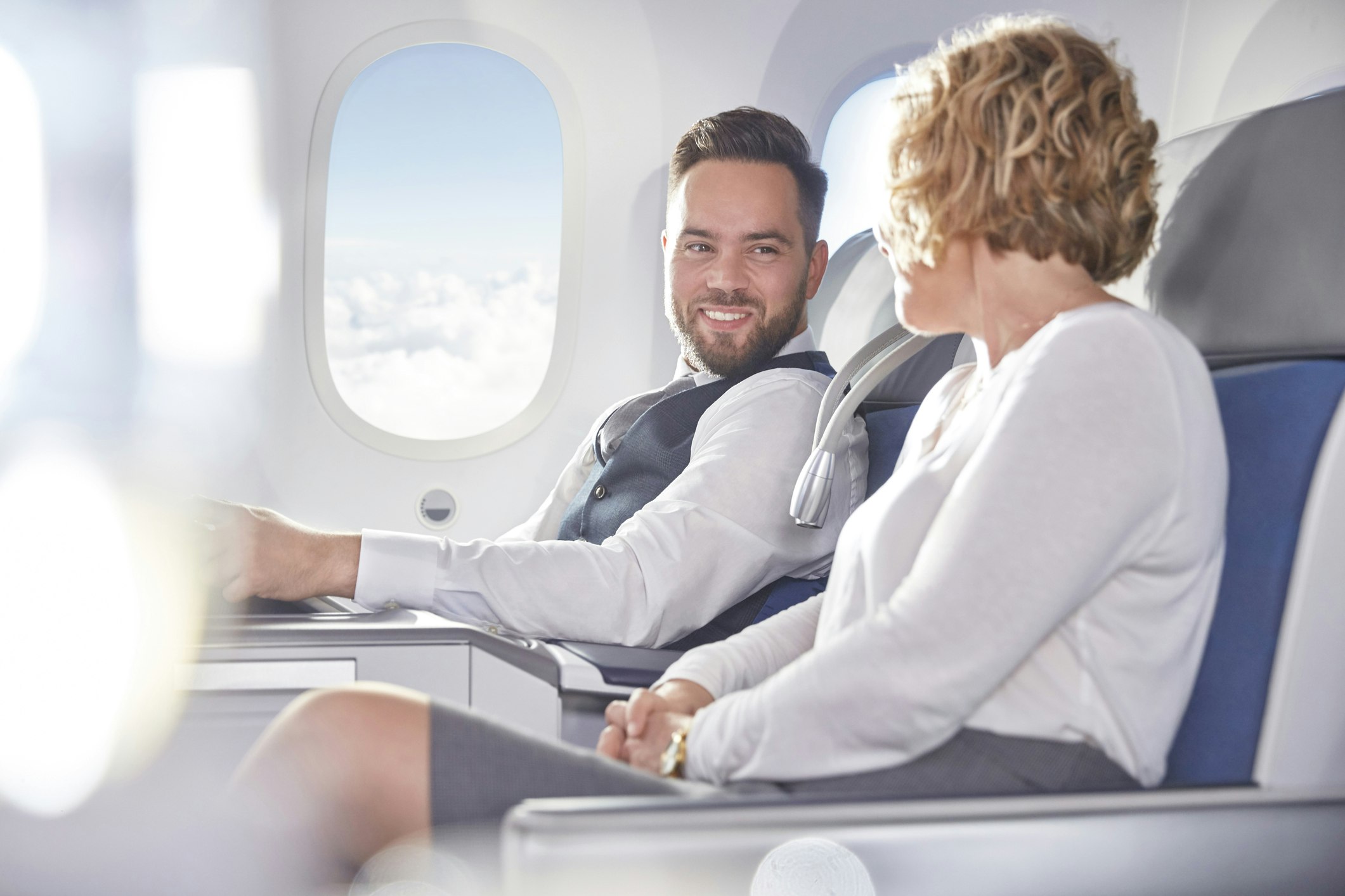Travel News - Smiling businessman and businesswoman talking on airplane