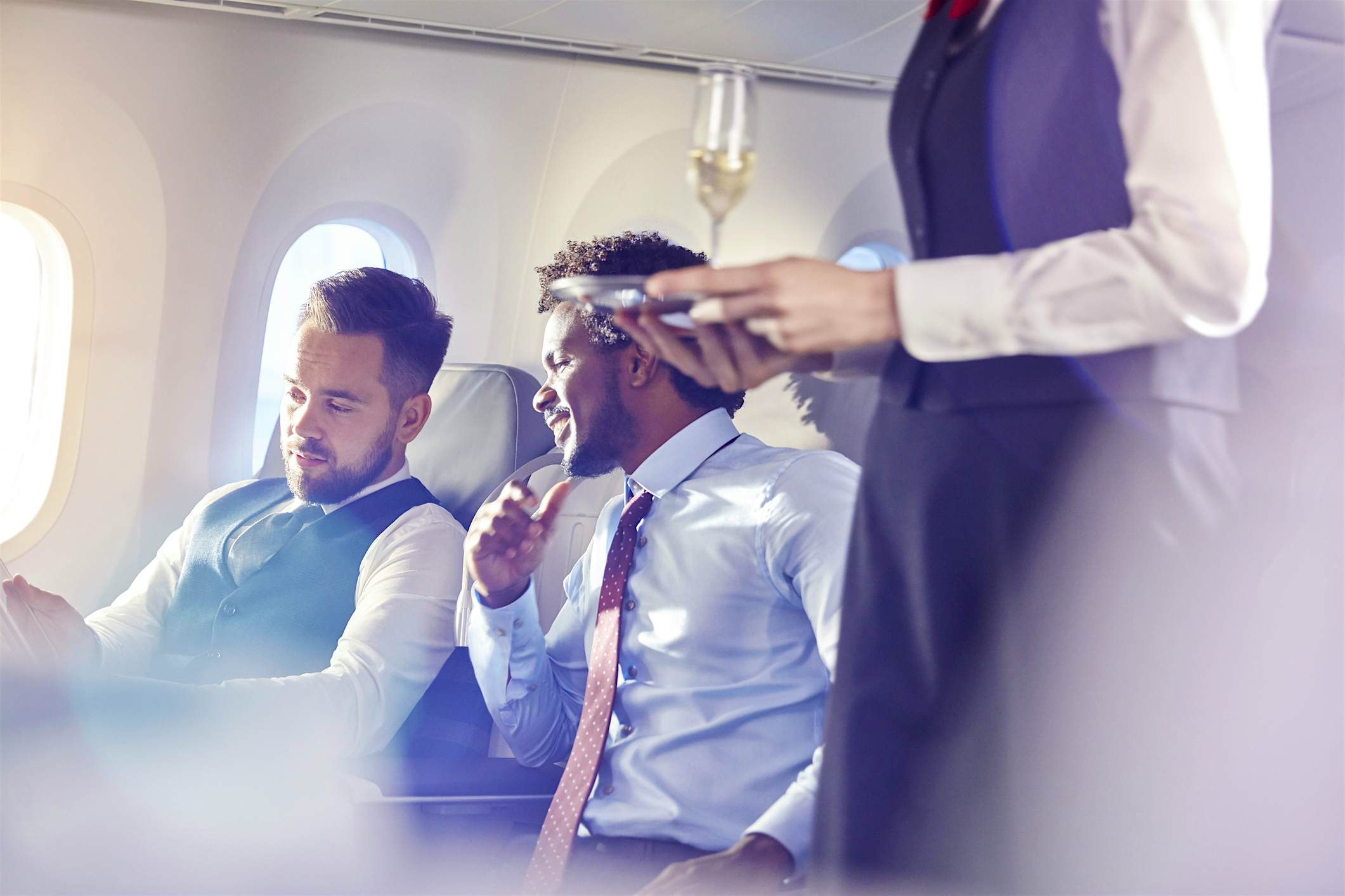 Travel News - Flight attendant serving champagne to businessmen in first class on airplane Travel News - Flight attendant serving champagne to businessmen in first class on airplane
