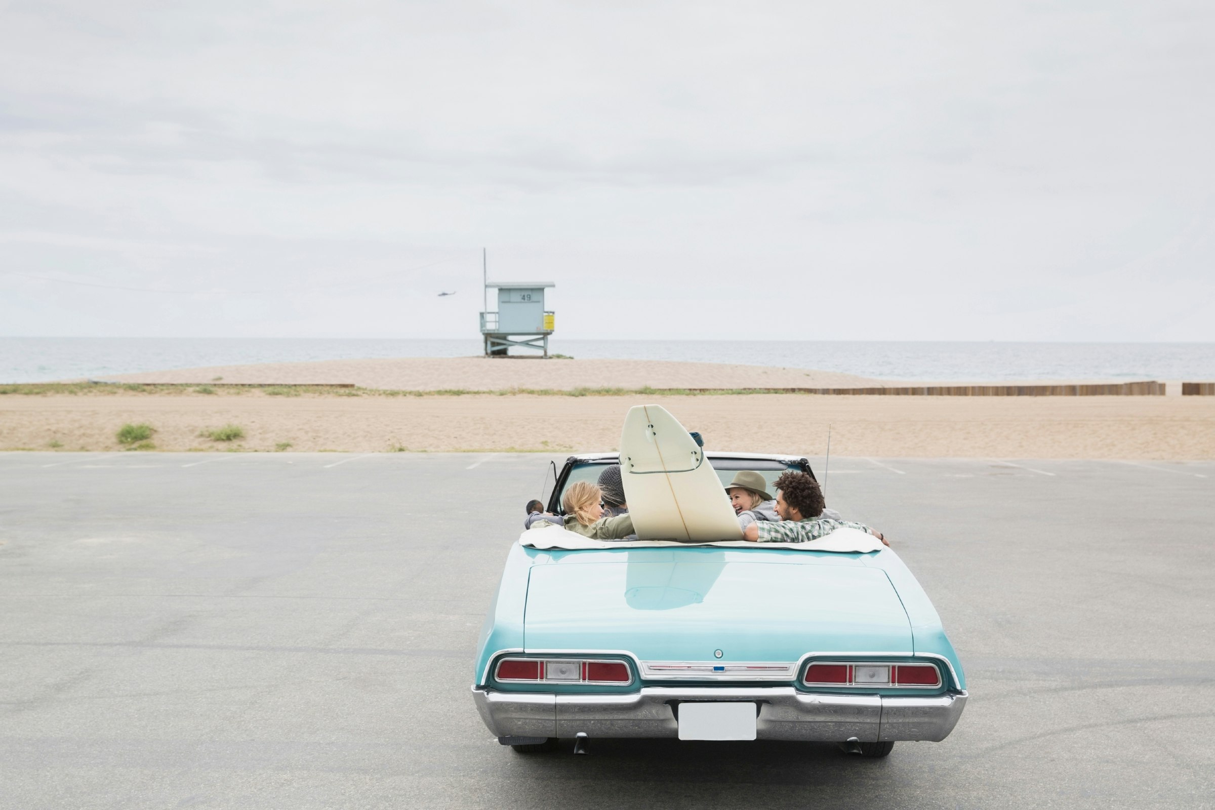 Travel News - Friends in convertible with surfboard arriving beach
