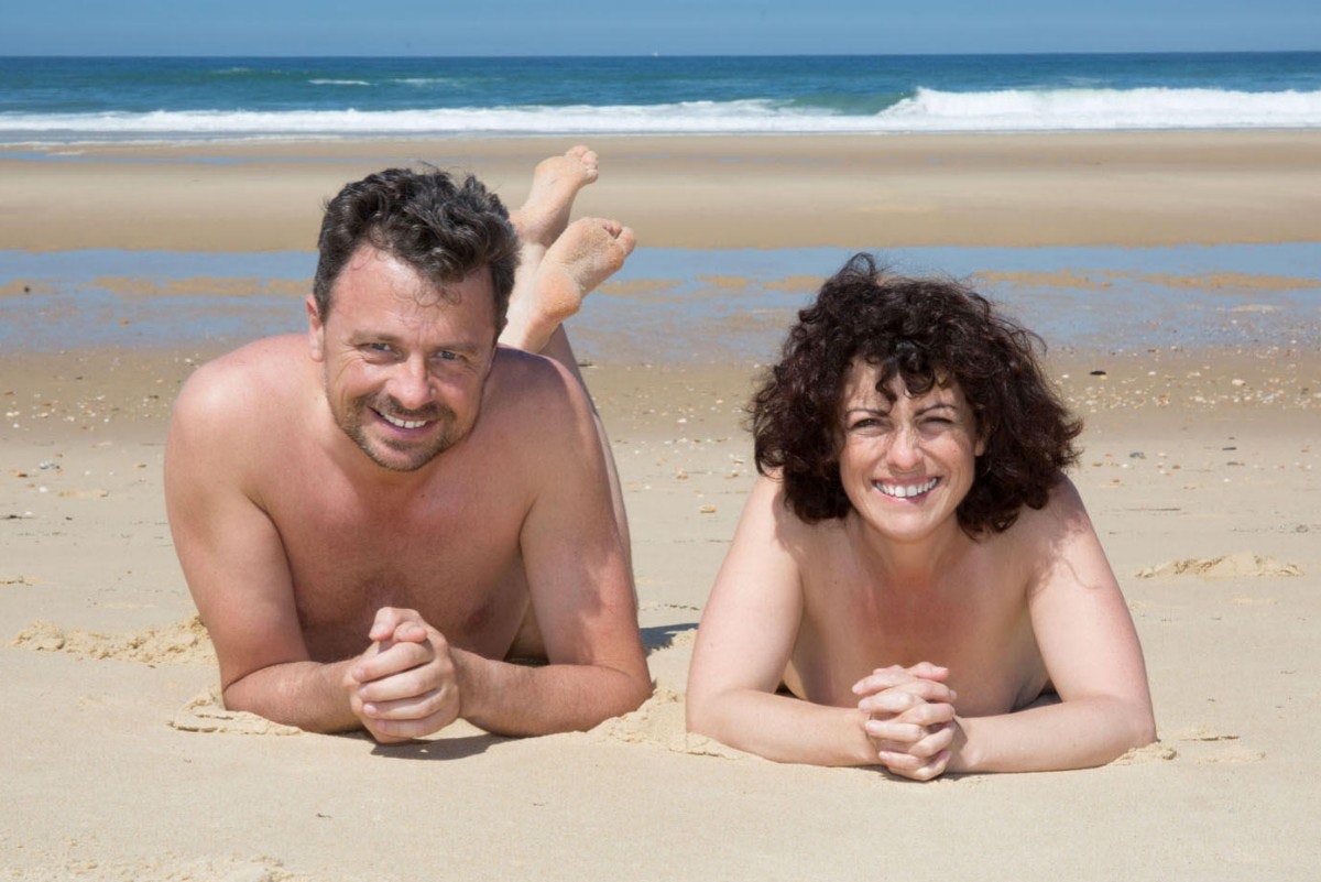 Travel News - Nude couple lying on warm sand by a sea and looking to camera