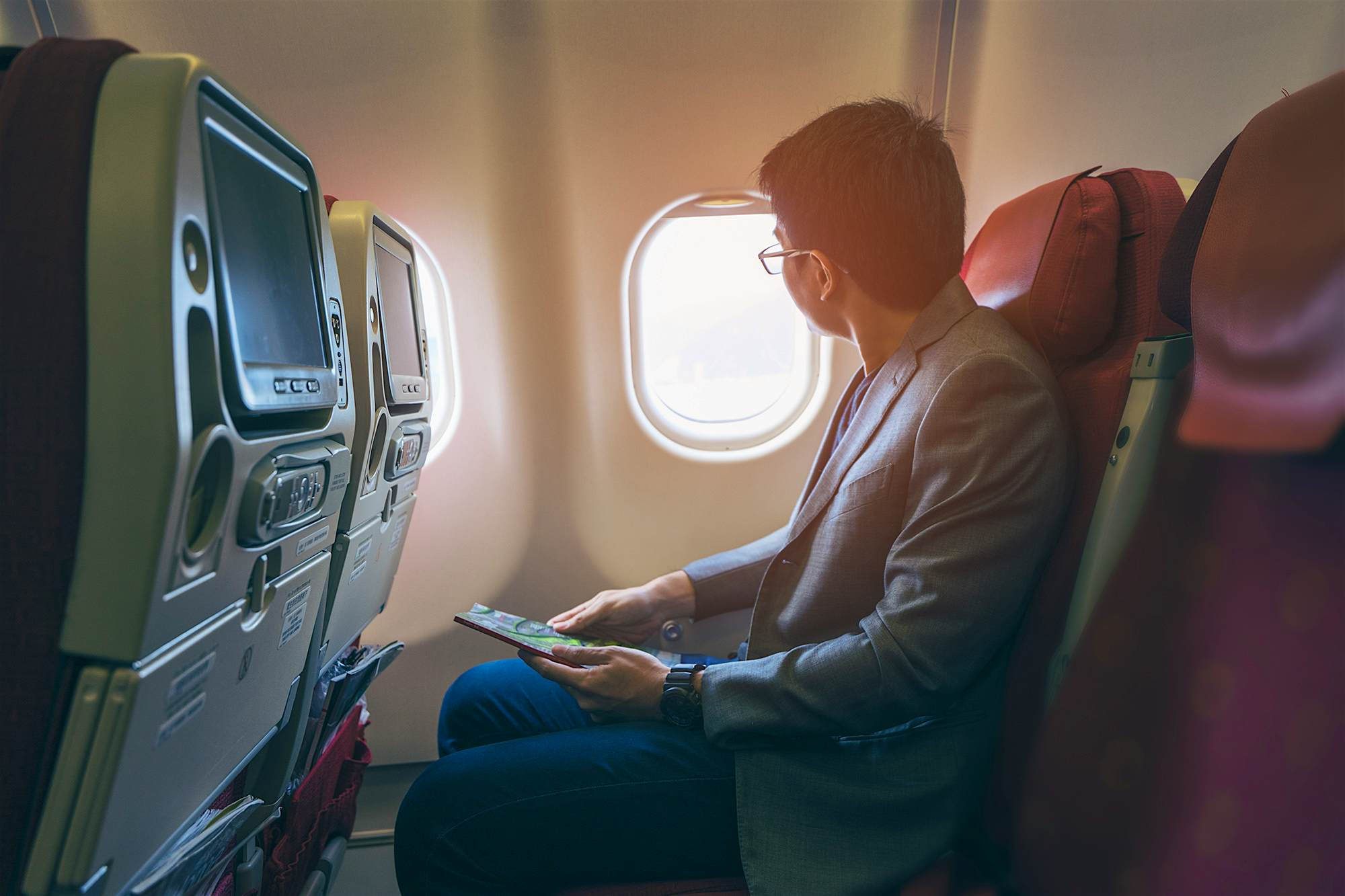 Travel News - Young asian business man smiling and looking view at window in airplane Are windlowless planes an option for airlines