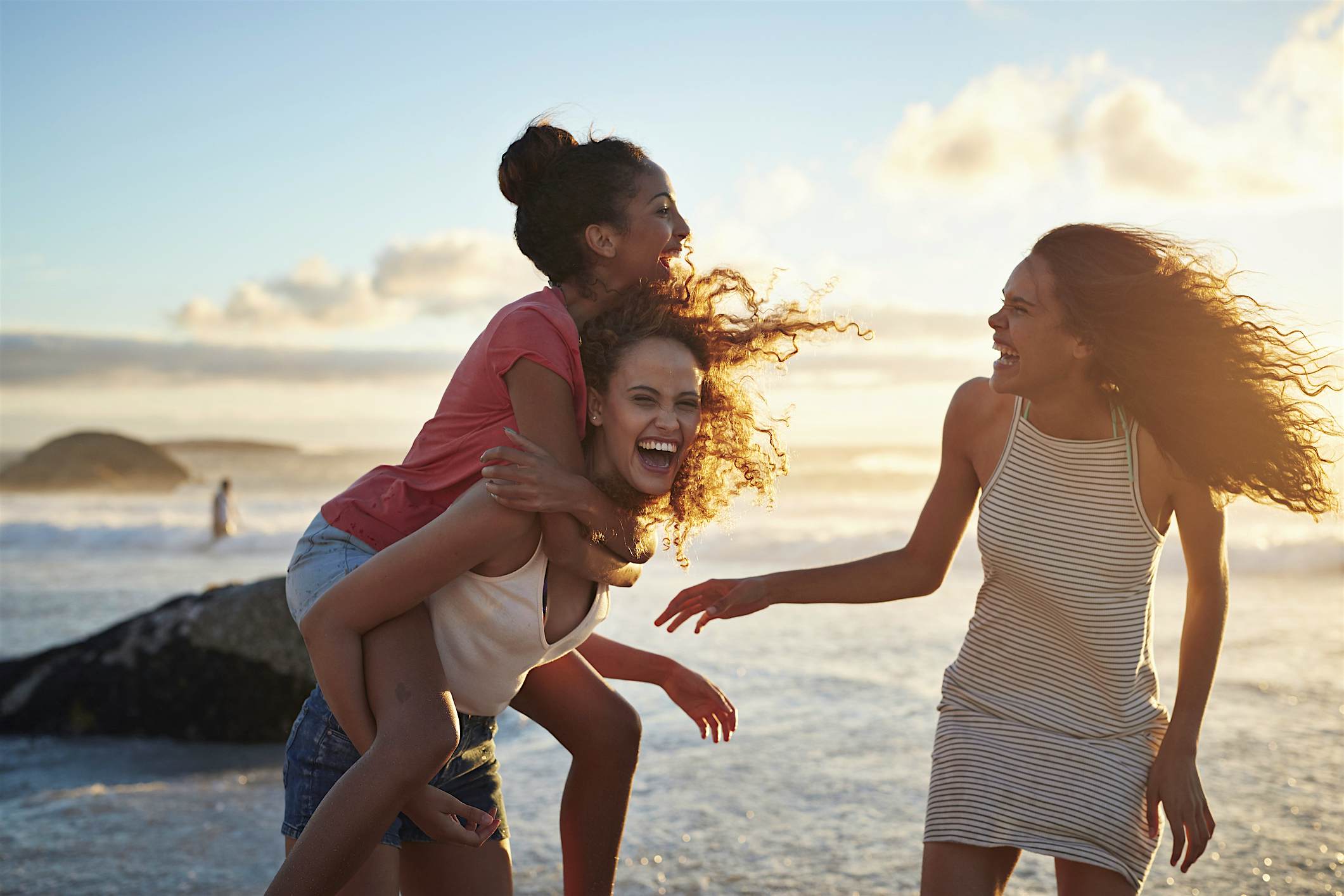 Travel News - Young women piggybacking on sandy beach Young women hanging out at the beach, at sunset