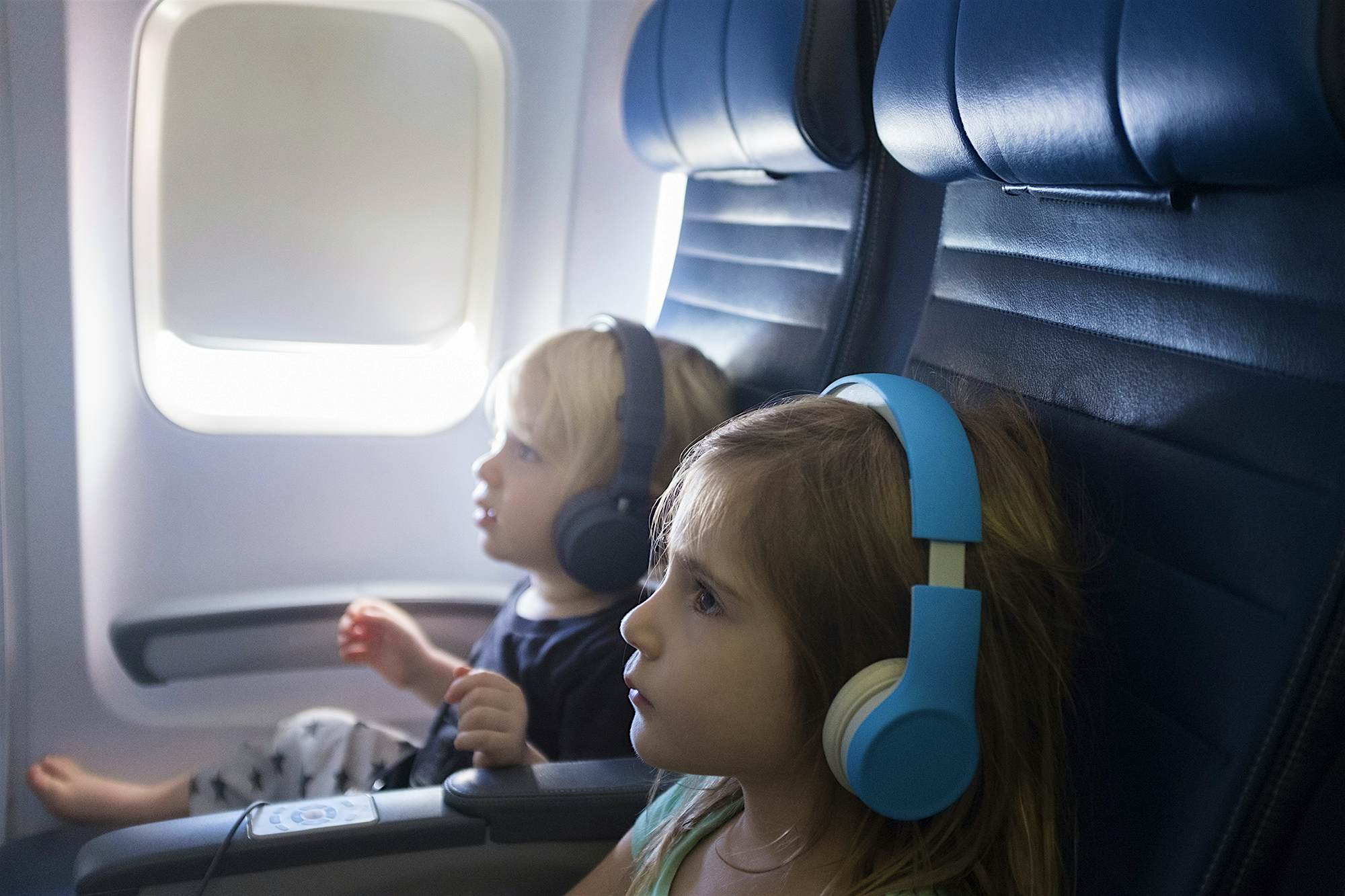Travel News - Boy (2-3) and girl (4-5) wearing headphones sitting in airplane Children watching videos on a plane