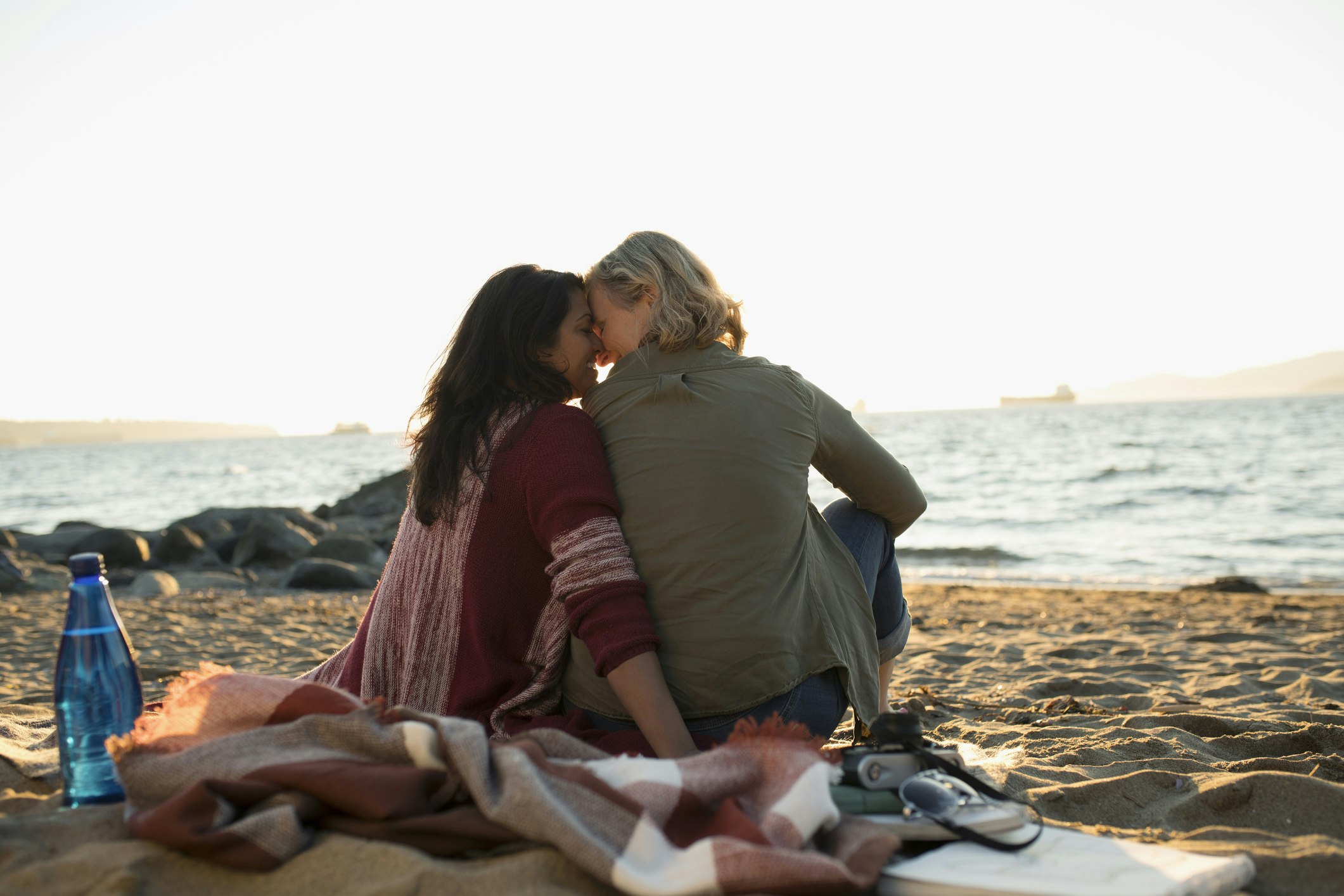 Travel News - Tender, affectionate lesbian couple sitting on blanket on ocean beach