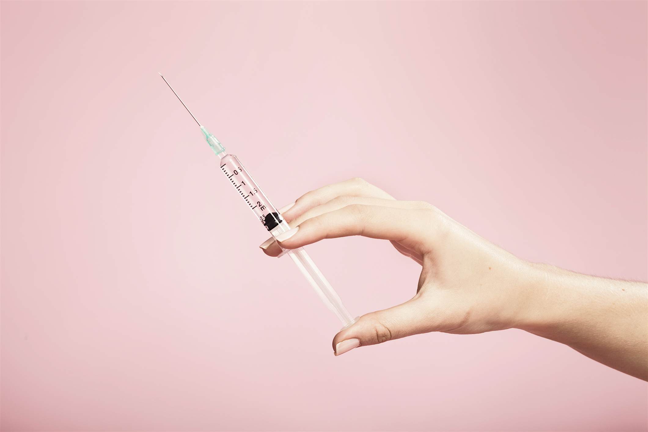 Travel News - Hand holding syringe in plain pink background Travel News - Hand holding syringe in plain pink background