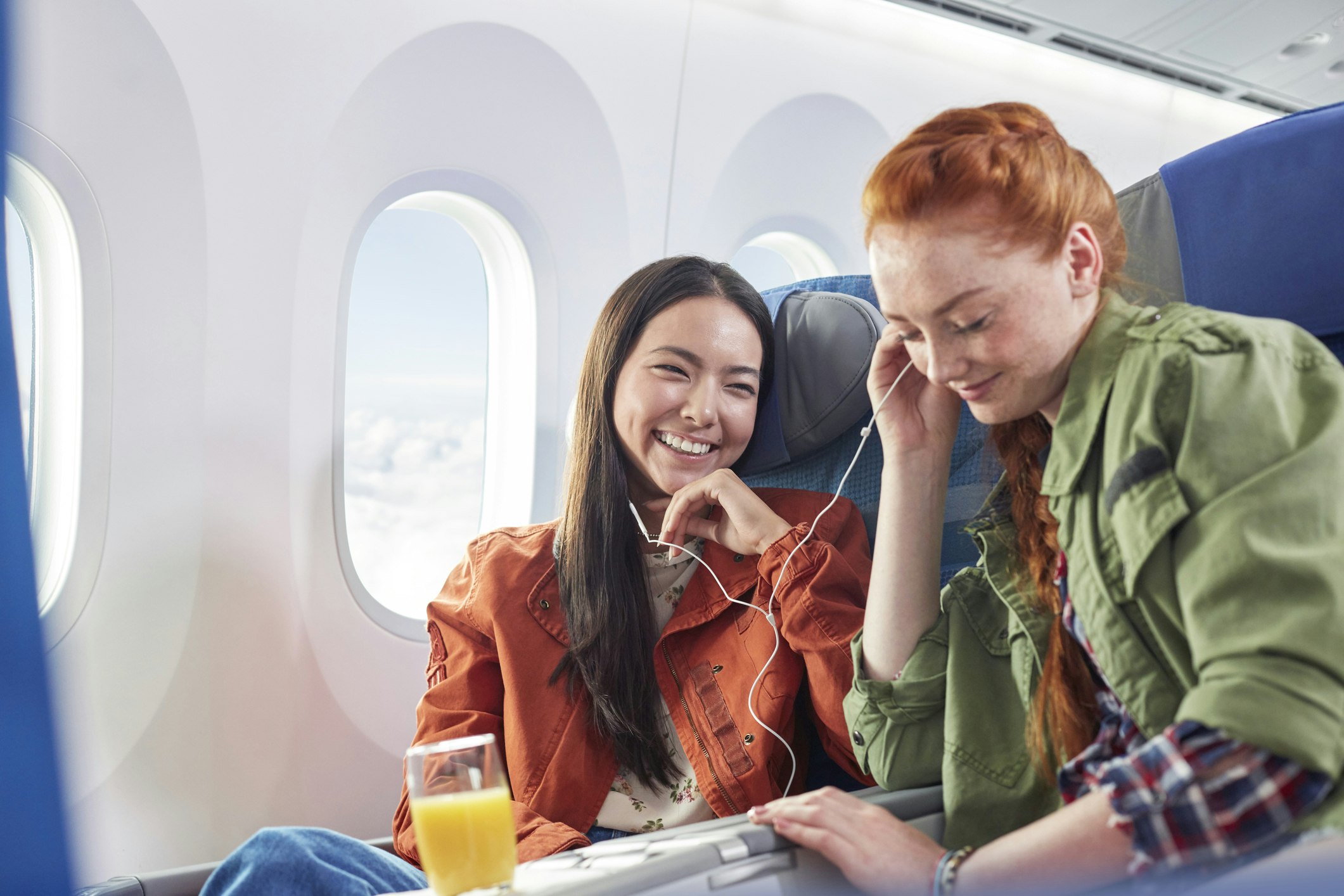 Young women friends sharing headphones, listening to music on airplane