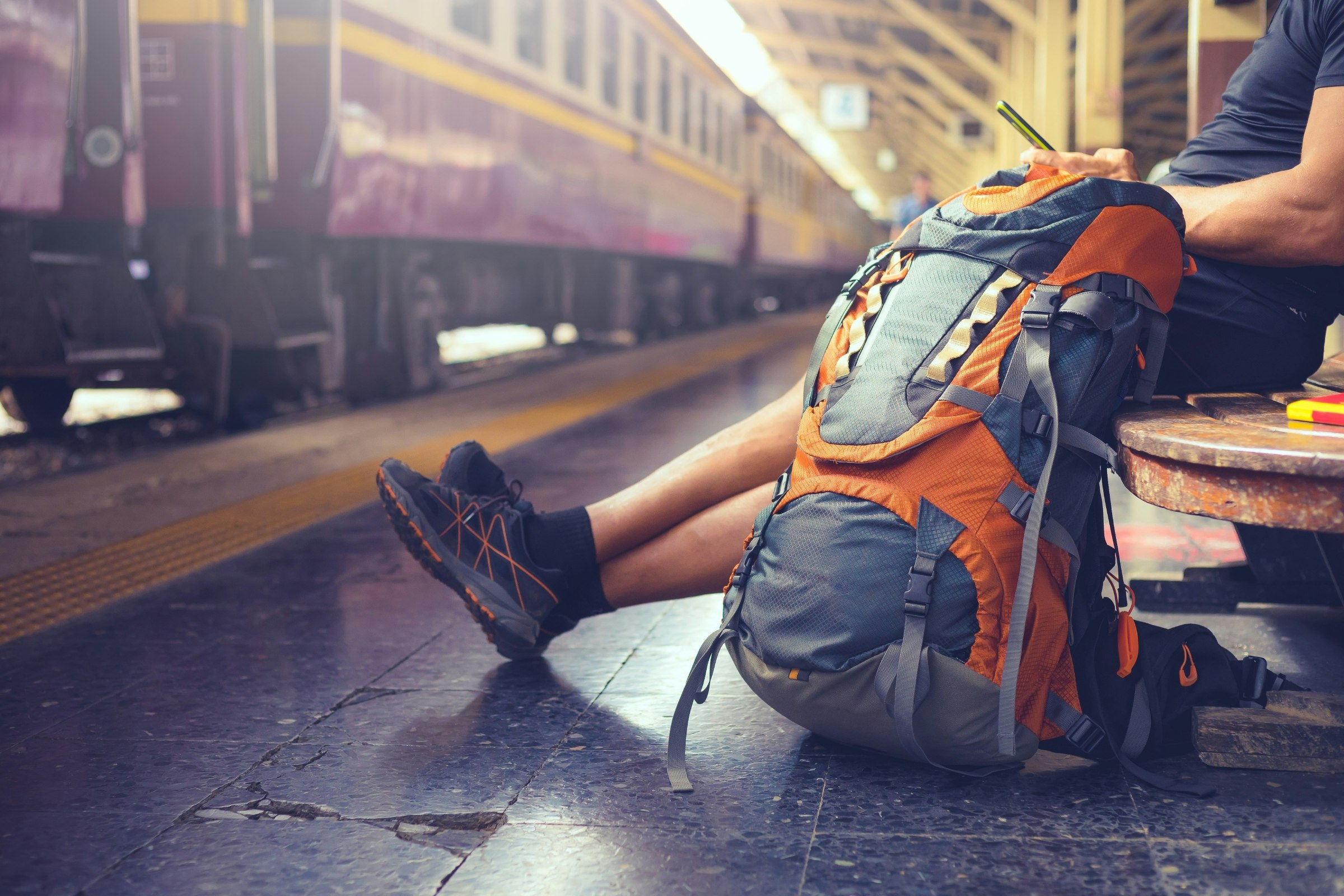 A backpacker uses his phone at a railway station while waiting for a train.