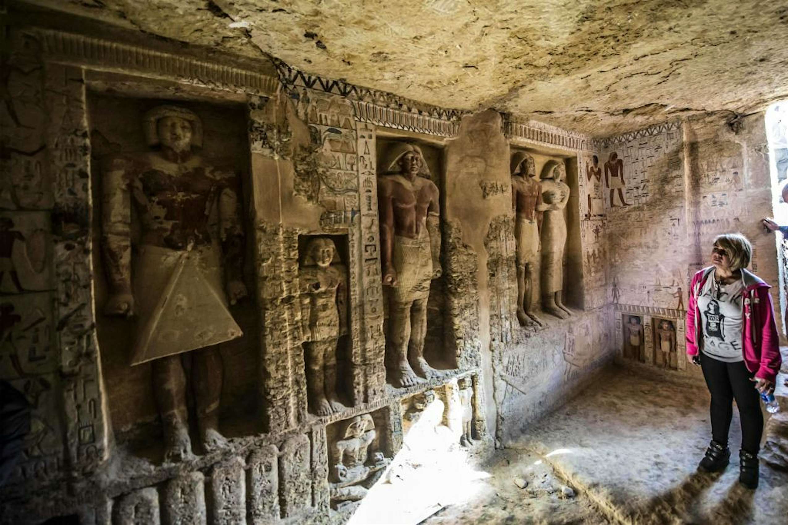  An image of a woman standing in an Ancient Egyptian tomb carved with statues and hieroglyphs in Nekropolis El-Assasif.