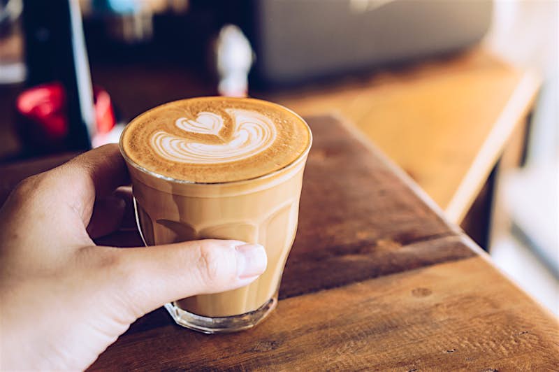 Travel News - Close-up of someone hand touching a shot glass of hot latte coffee in the cafe. Travel News - Close-up of someone hand touching a shot glass of hot latte coffee in the cafe.