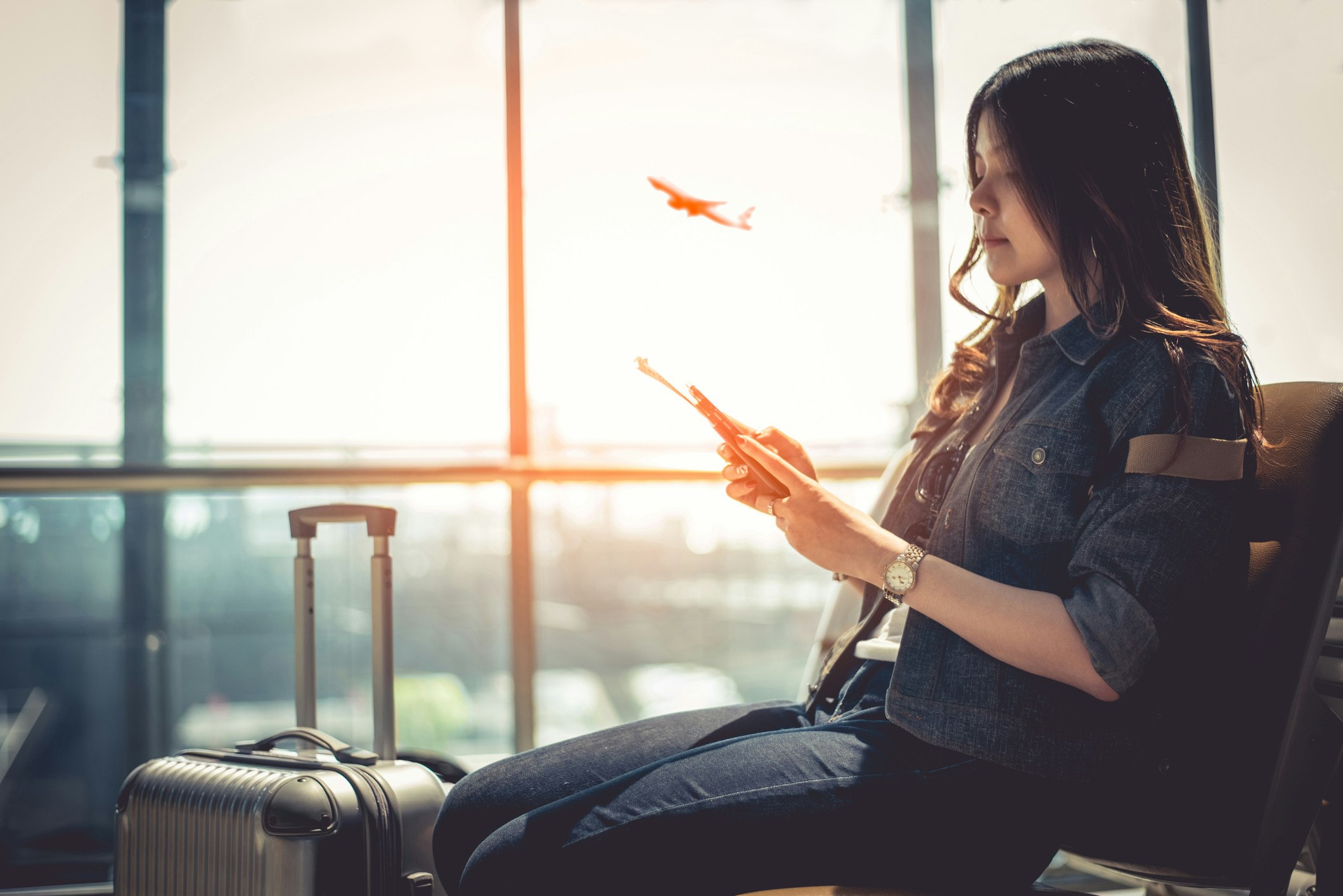 Travel News - Woman Using Smart Phone While Sitting At Departure Area In Airport