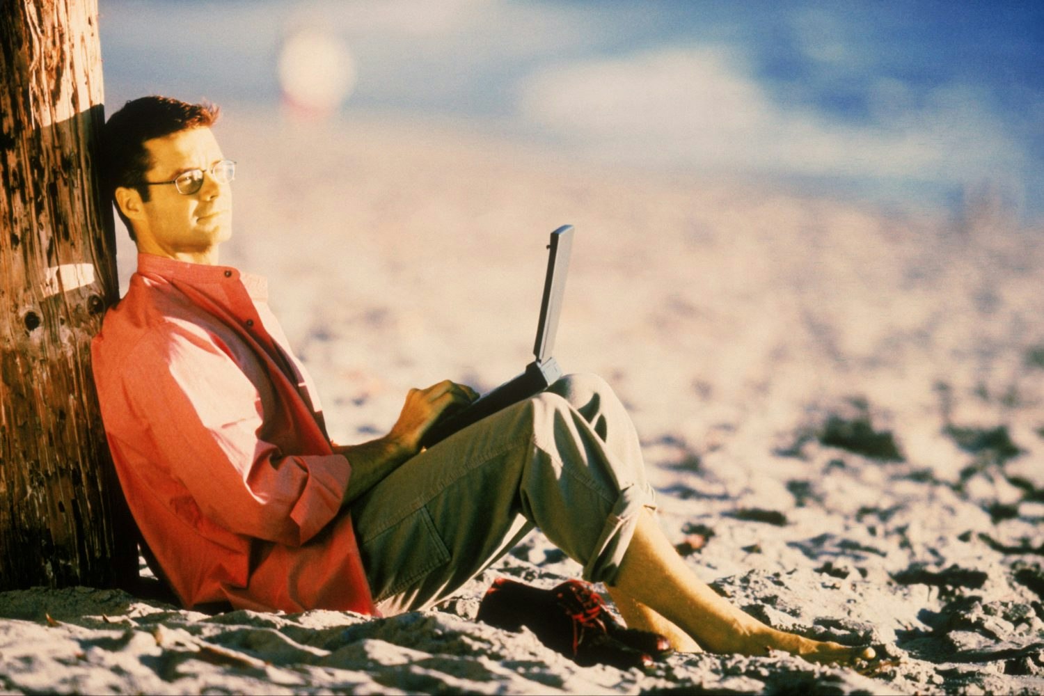 A young man sitting against a tree holding a laptop