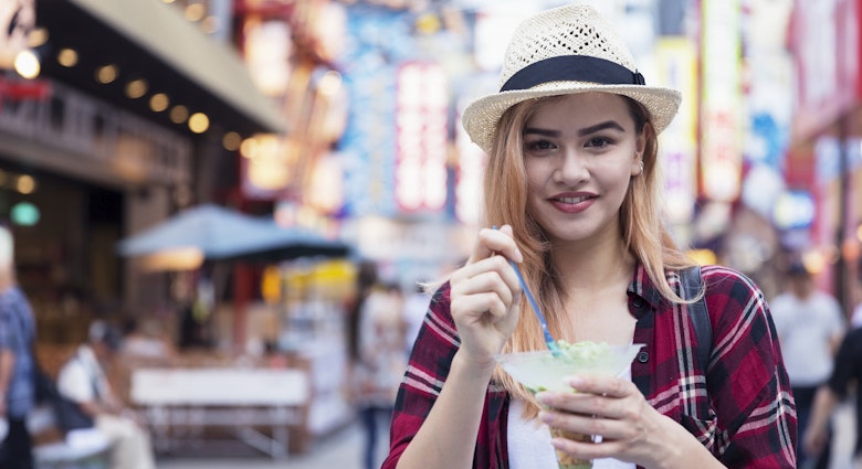 Travel News - Young tourist enjoying ice cream as she walks down Shinsekai Street