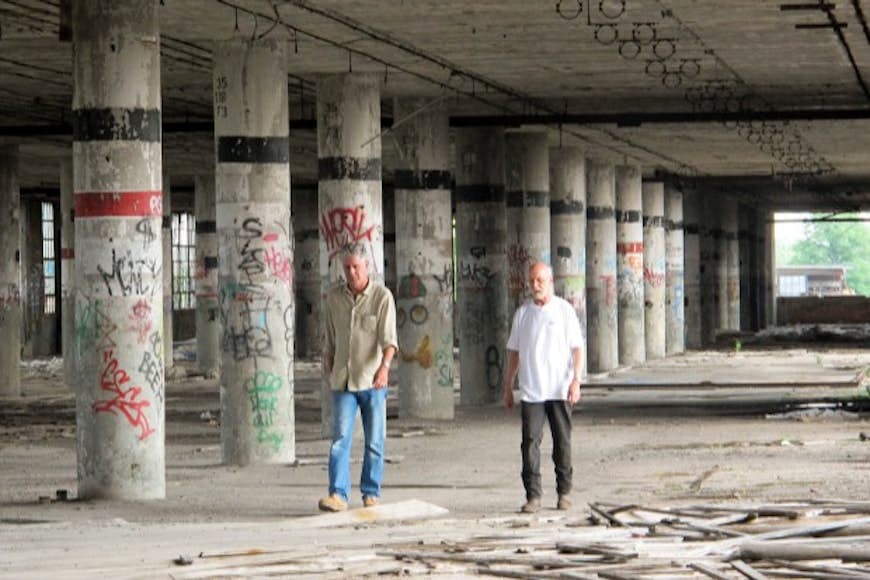 Anthony Bourdain walking through abandoned building with an another man in Detroit.