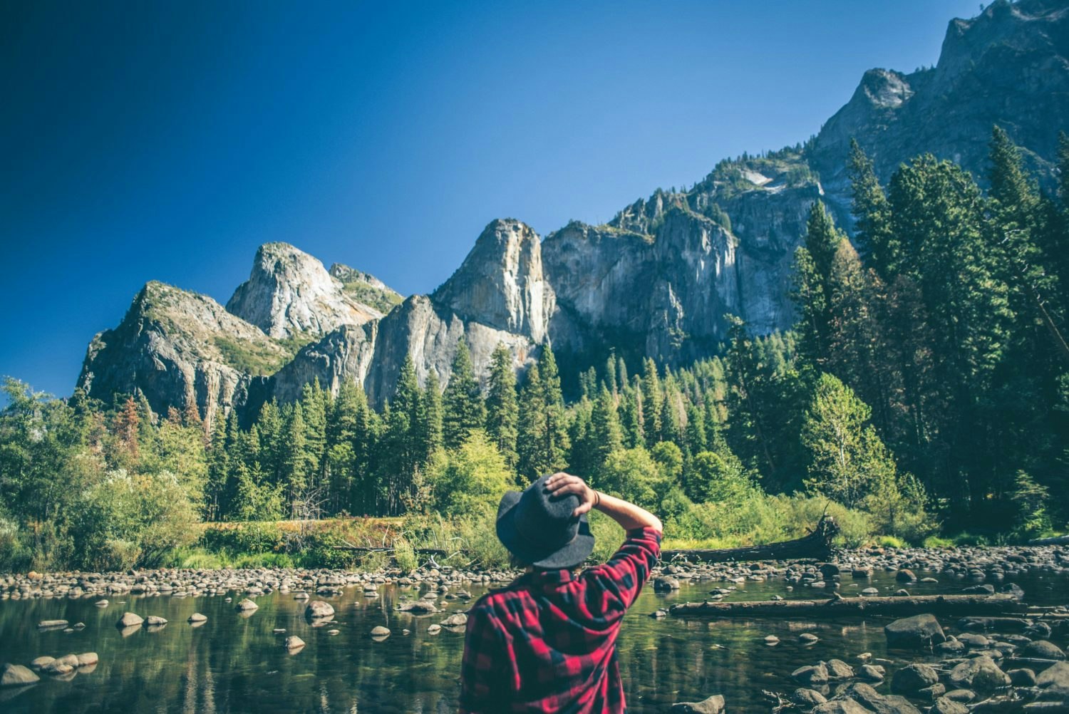 A young woman walking along a river in a majestic landscape.